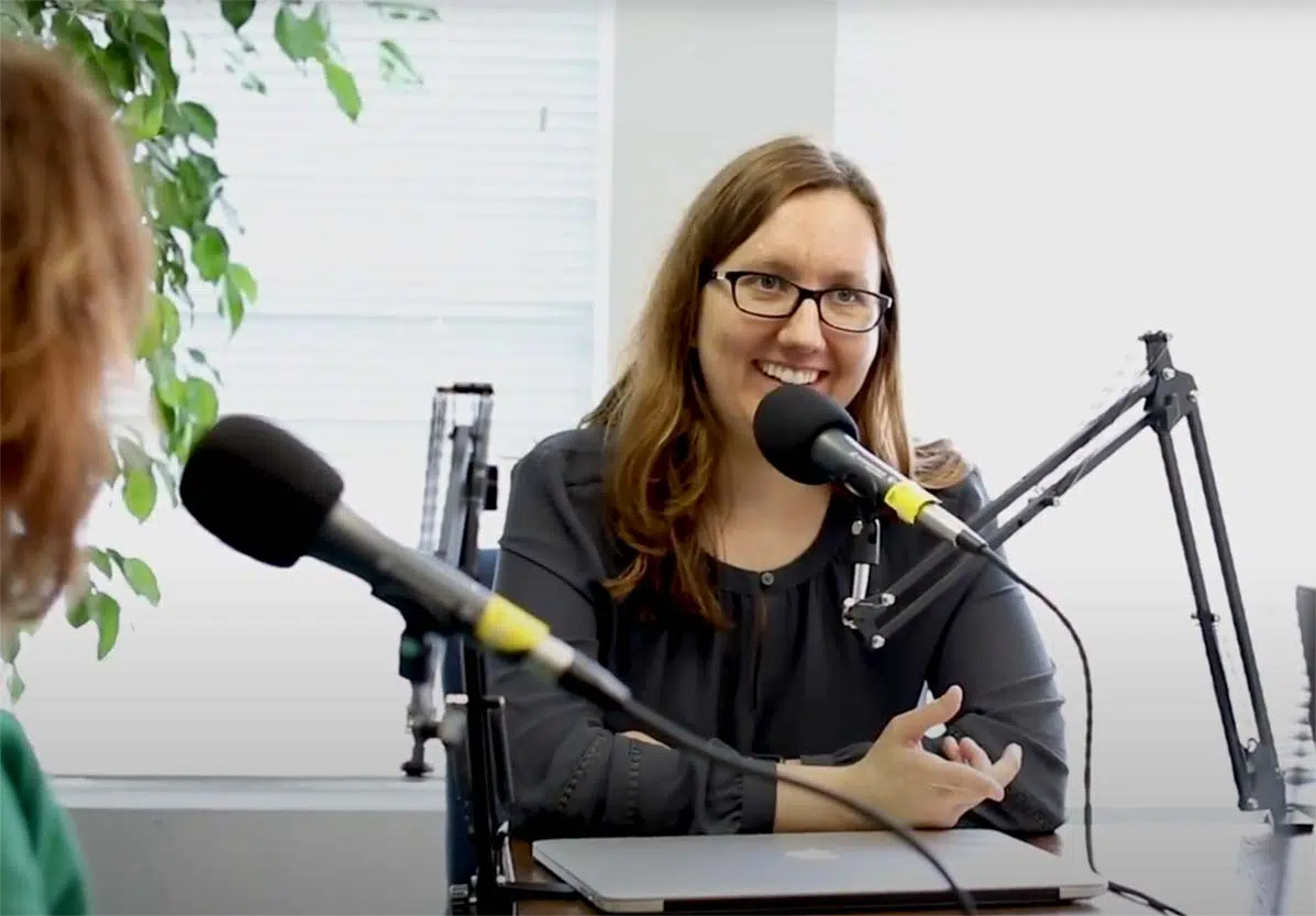 Sarah smiles while sitting in front of a microphone recording a podcast.