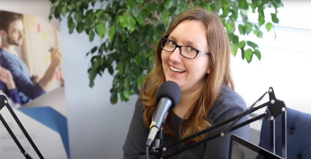 Sarah speaks into a microphone while sitting at a table where she is recording a podcast.