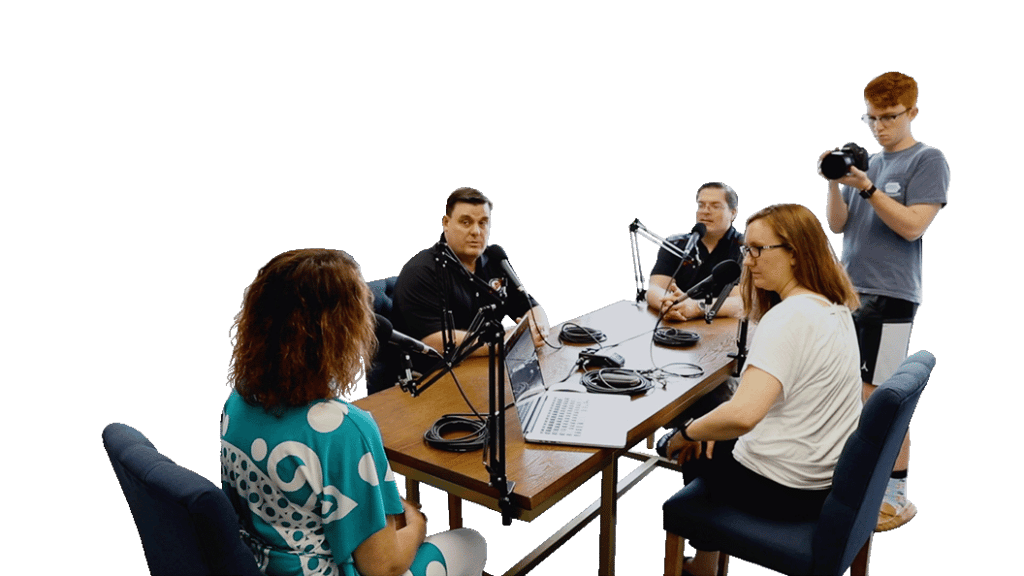 A group of people sit around a table with microphones to record a podcast episode.