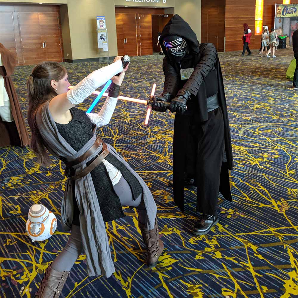 Cosplayers dressed as Rey and Kylo Ren battling with lightsabers.